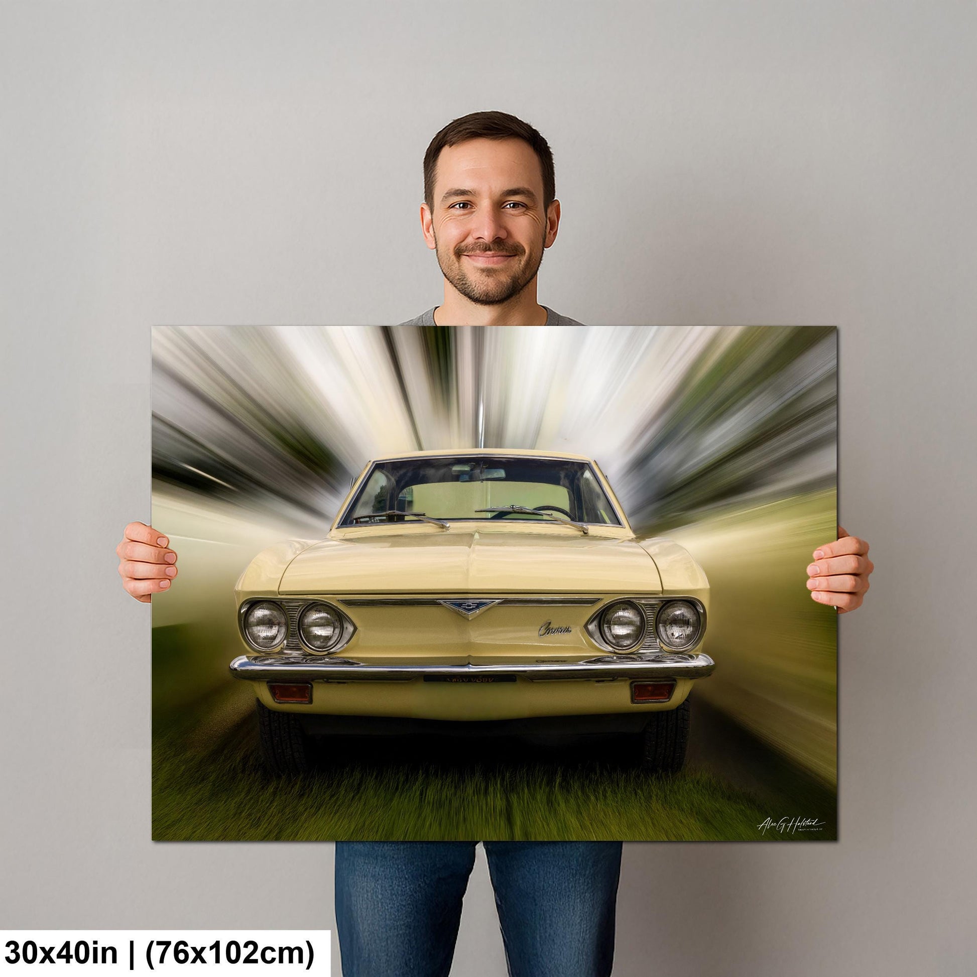 A man is holding up a framed print of a yellow car with a blurred background, creating a sense of motion.