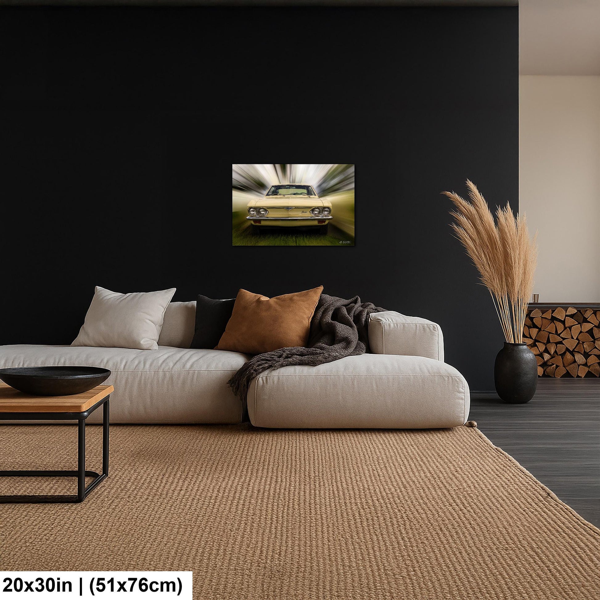 a living room with a large, plush white sofa and a wooden coffee table. Above the sofa, there is a framed picture of a yellow car, and a vase with dried flowers is placed on the floor next to the sofa. The walls of the room are painted black, and there is a rug on the floor.